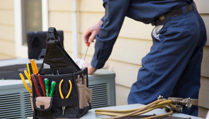 HVAC technician inspecting an older air conditioning unit for repair or replacement.